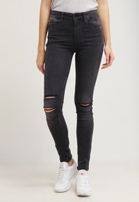 Svarta tajta jeans i denim, med slitna knäkår och smal passform, hög midja och subtilt röd söm på frampocket.