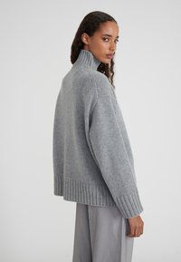Pull à col roulé gris clair avec ourlet et poignets côtelés, fabriqué à partir d'une maille texturée ; coupe ample avec couture d'épaule tombante.