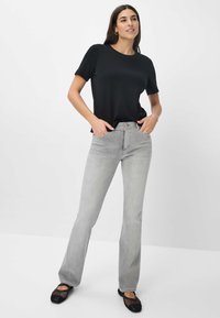 Schwarzes Kurzarmoberteil kombiniert mit hellgrauen, ausgestellten Jeans, die einen klassischen Schnitt und ein minimalistisches Design aufweisen. Schwarze Mesh-Ballerinas vervollständigen den Look.
