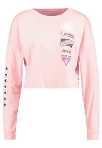 Rosa kortärmad långärmad t-shirt i bomull, med svarta stjärndetaljer på ärmarna och flera tryckta logotyper på framsidan.