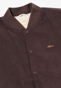 Dark brown corduroy jacket with a ribbed collar, two buttons, and embroidered "Blkvis" logo in gold on the chest.