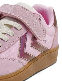 Nahaufnahme eines rosa Sneakers mit Wildlederriemen, weißen Schnürsenkeln, strukturiertem Stoff, braunen Chevron-Streifen und Gummisohle.