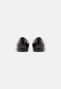 Des mocassins en cuir verni noir présentent un design épuré avec un bout arrondi, des coutures minimales et un talon plat et brillant.