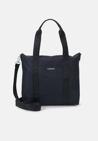 Marinblå nylon tote-väska med en strukturerad form, som har dubbla handtag och ett justerbart axelband. Logodetalj på banden.