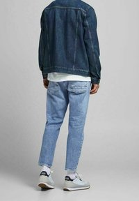 Jeansjacka i mörkblått, ljusblå avsmalnande jeans och vita sneakers med grå och svarta accenter. Bakre vy som visar fickdetaljer.