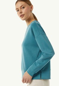 Turkusowy sweatshirt z długimi rękawami, okrągłym dekoltem, żebrowanym dołem i bocznymi rozcięciami. Wykonany z miękkiego, teksturowanego materiału.