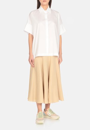 Camicia bianca a maniche corte con bottoni frontali, abbinata a una gonna beige a campana e sneakers pastello con accenti di design discreti.