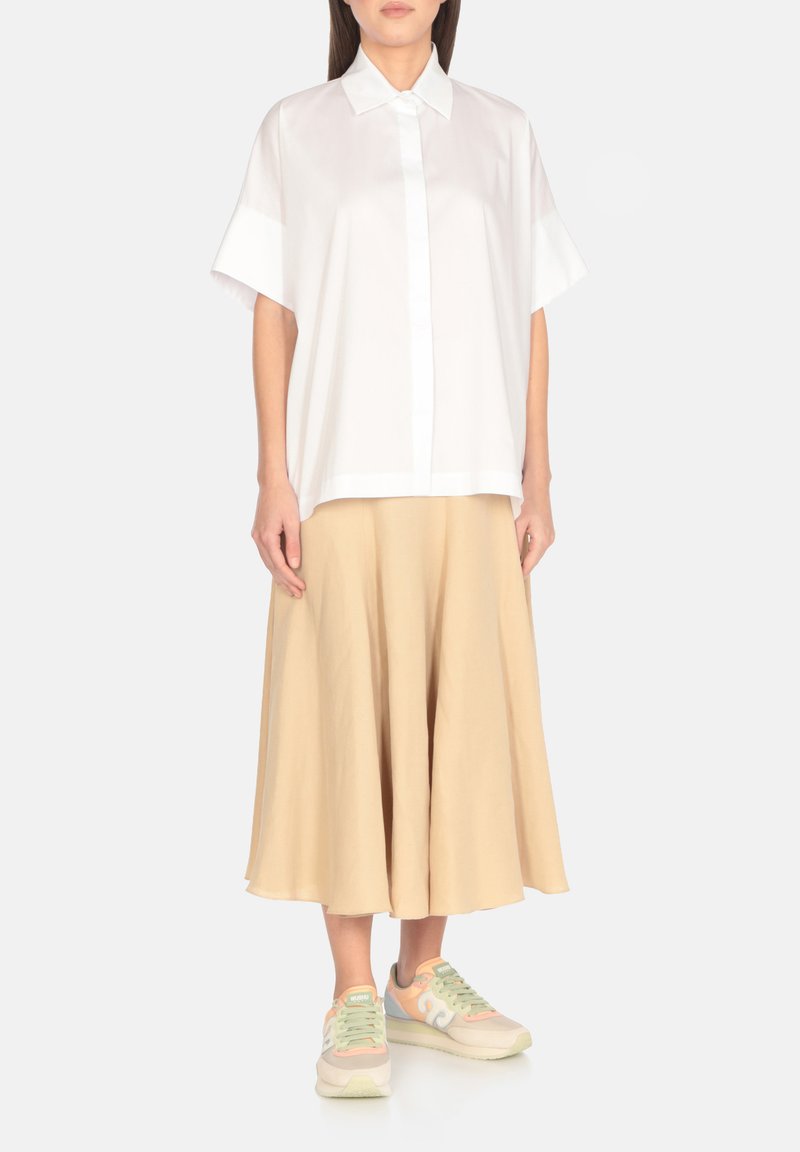 Camicia bianca a maniche corte con bottoni frontali, abbinata a una gonna beige a campana e sneakers pastello con accenti di design discreti.