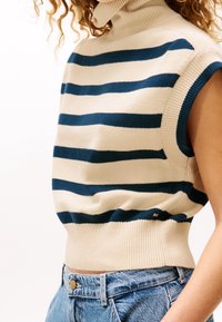 Sweter z dzianiny z golfem w kremowo-granatowe paski, krótkie rękawy i prążkowane wykończenia. Noszony na wysokich jeansowych szortach.