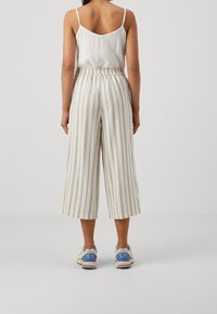 Vita linnebyxor i croppad modell med beige vertikala ränder, elastisk midja och fickor, kombinerat med sportiga sneakers i dämpade nyanser.