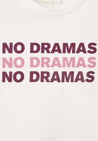 Bílá látka s opakovanou frází "NO DRAMAS" tučným písmenem a velkými písmeny, dvakrát v tmavě vínové a jednou ve světle růžové, uprostřed.