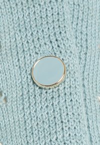 Litet runt spegel med en gyllene kant placerad på en ljusblå stickad tyg med vertikal ribbstruktur.