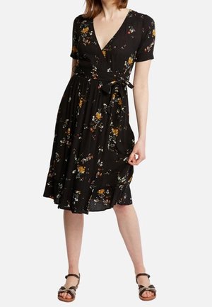 Robe à fleurs noire avec manches courtes, décolleté en v, et lien de taille. Elle présente une jupe fluide avec des volants et des motifs de fleurs multicolores.