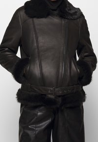 Brun läderjacka med krage och manschetter i konstpäls, med dragkedjestängning och matchande bälte. Slät yta med skräddarsydd design.