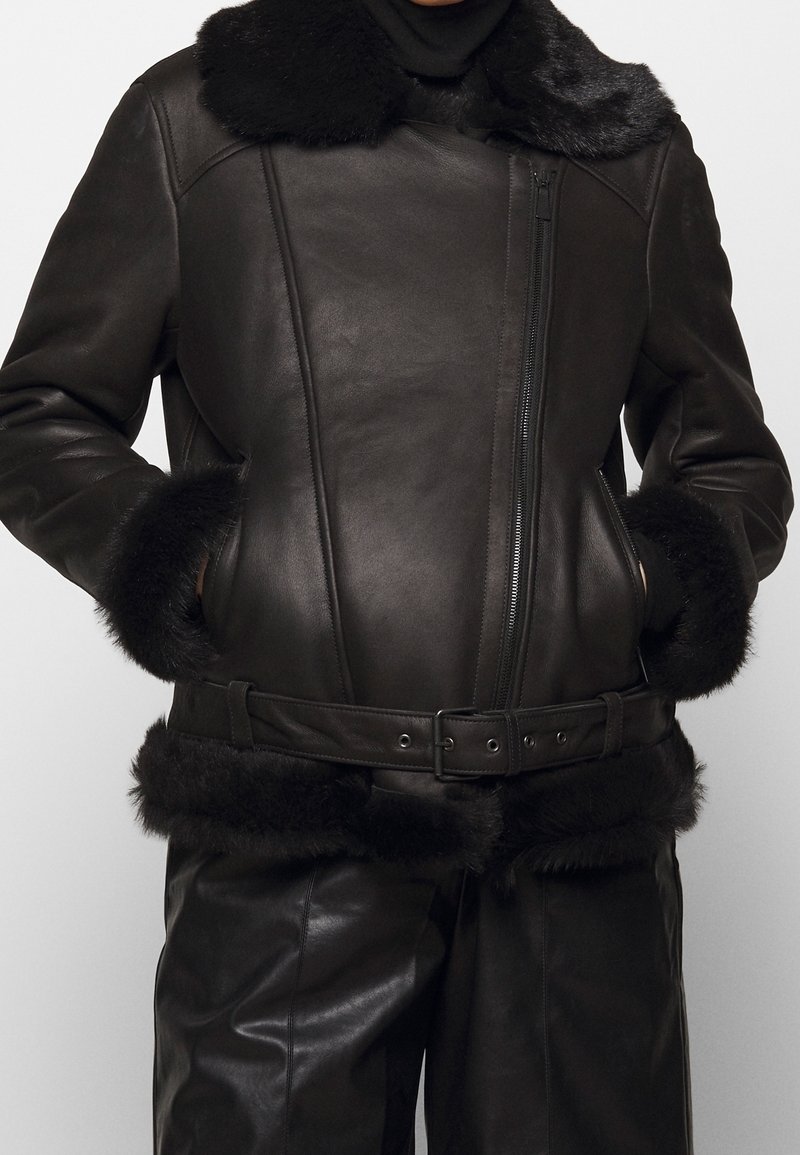 Brun läderjacka med krage och manschetter i konstpäls, med dragkedjestängning och matchande bälte. Slät yta med skräddarsydd design.