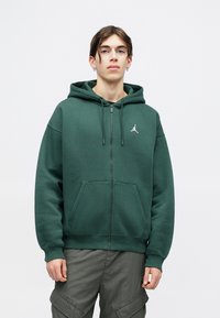 Felpa verde con zip, realizzata in morbido tessuto, dotata di una tasca a marsupio, stringhe e un piccolo logo ricamato sul petto.