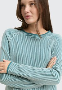 Turkusowy sweter w paski z okrągłym dekoltem i ściągaczami. Wzór składa się z naprzemiennych jasnych i ciemnych pasków.