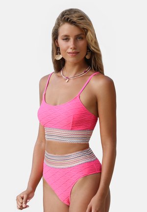 Jonge vrouw met lang haar die een roze textuurbikini draagt met meerkleurige gestreepte banden, een schelpenketting en hangende oorbellen.