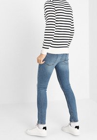 Jeans ajustados de color azul claro con una textura suave y diseño de cinco bolsillos, combinados con una camisa de manga larga a rayas en blanco y negro y zapatillas blancas.