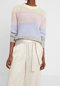 Meerkleuren gebreide trui met strepen in pastelgeel, rose en blauw; gecombineerd met lichtbeige, hoge taille, geplooide broek.