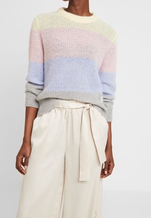 Meerkleuren gebreide trui met strepen in pastelgeel, rose en blauw; gecombineerd met lichtbeige, hoge taille, geplooide broek.