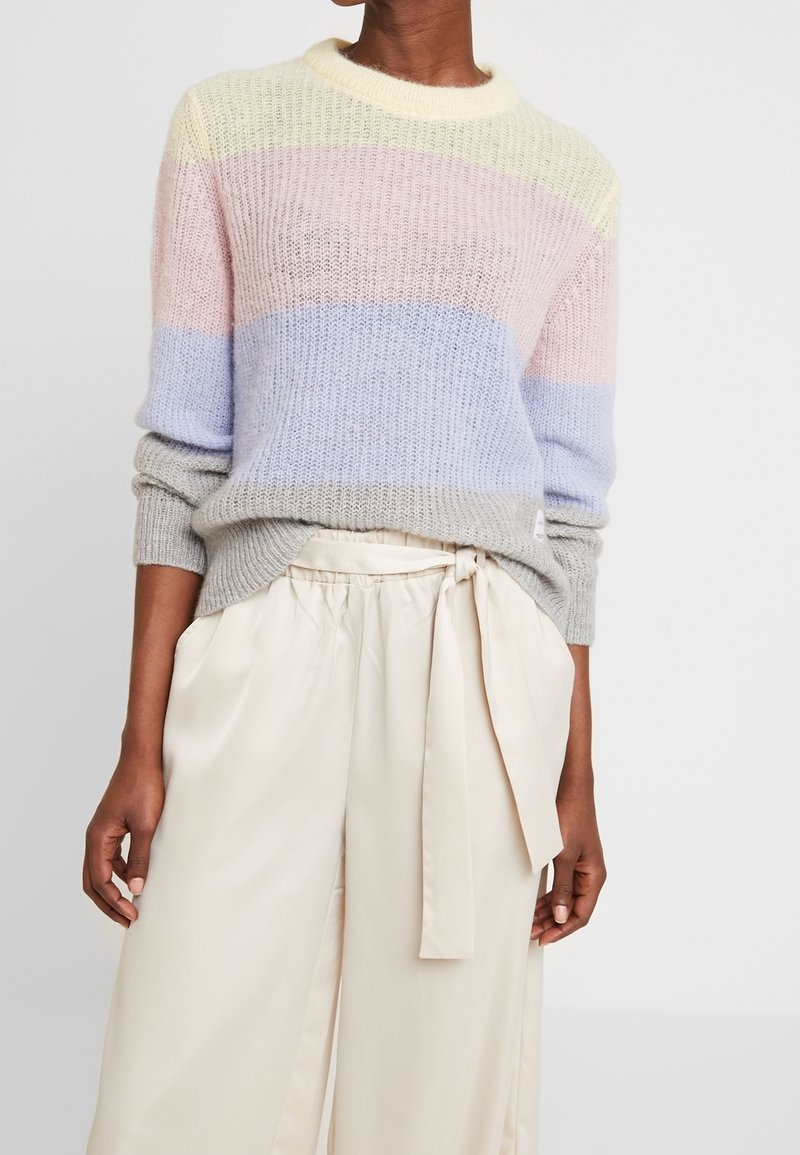 Meerkleuren gebreide trui met strepen in pastelgeel, rose en blauw; gecombineerd met lichtbeige, hoge taille, geplooide broek.