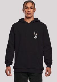 Felpa nera con tasca a marsupio e polsini a coste, con una grafica di Bugs Bunny sul lato sinistro del petto. Il materiale sembra morbido e confortevole.