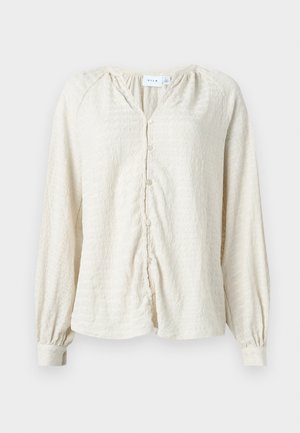 Blusa de manga larga de textura crema con botones en la parte delantera y puños con elasticidad, que presenta un cuello en V y hombros fruncidos.