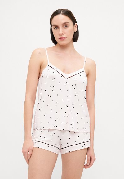 Svijetloružasti kokon sa majicom na bretele s tankim trakama i uzorkom crnih srca, uparen s odgovarajućim šortsevima s crnim obrubima.