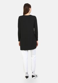 Schwarze Langarmtunika mit abgerundetem Saum, kombiniert mit weißen geraden Hosen und schwarzen Sneakers mit Akzenten. Einfaches und lässiges Design.