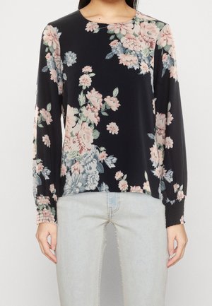 Czarna bluzka z długim rękawem z różowo-szarym kwiatowym wzorem, okrągłym dekoltem i marszczonymi mankietami, w połączeniu z jasnoniebieskimi dżinsami.