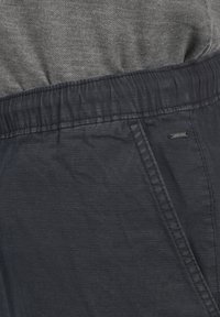 Material de culoare gri închis, ușor, cu un finisaj texturat. Curea elastică cu detalii pliate. Buzunar lateral vizibil cu branding subtil.