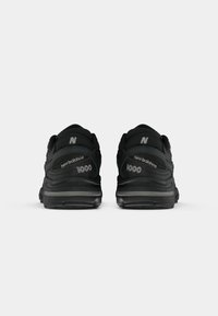Ténis de desporto pretos com um colarinho acolchoado, parte superior texturizada e marca "new balance". Detalhes refletivos e uma distintiva almofada de calcanhar.