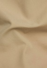 Tessuto beige testurizzato con pieghe sottili, finitura liscia e un motivo di tessitura uniforme, che mostra un colore neutro chiaro.
