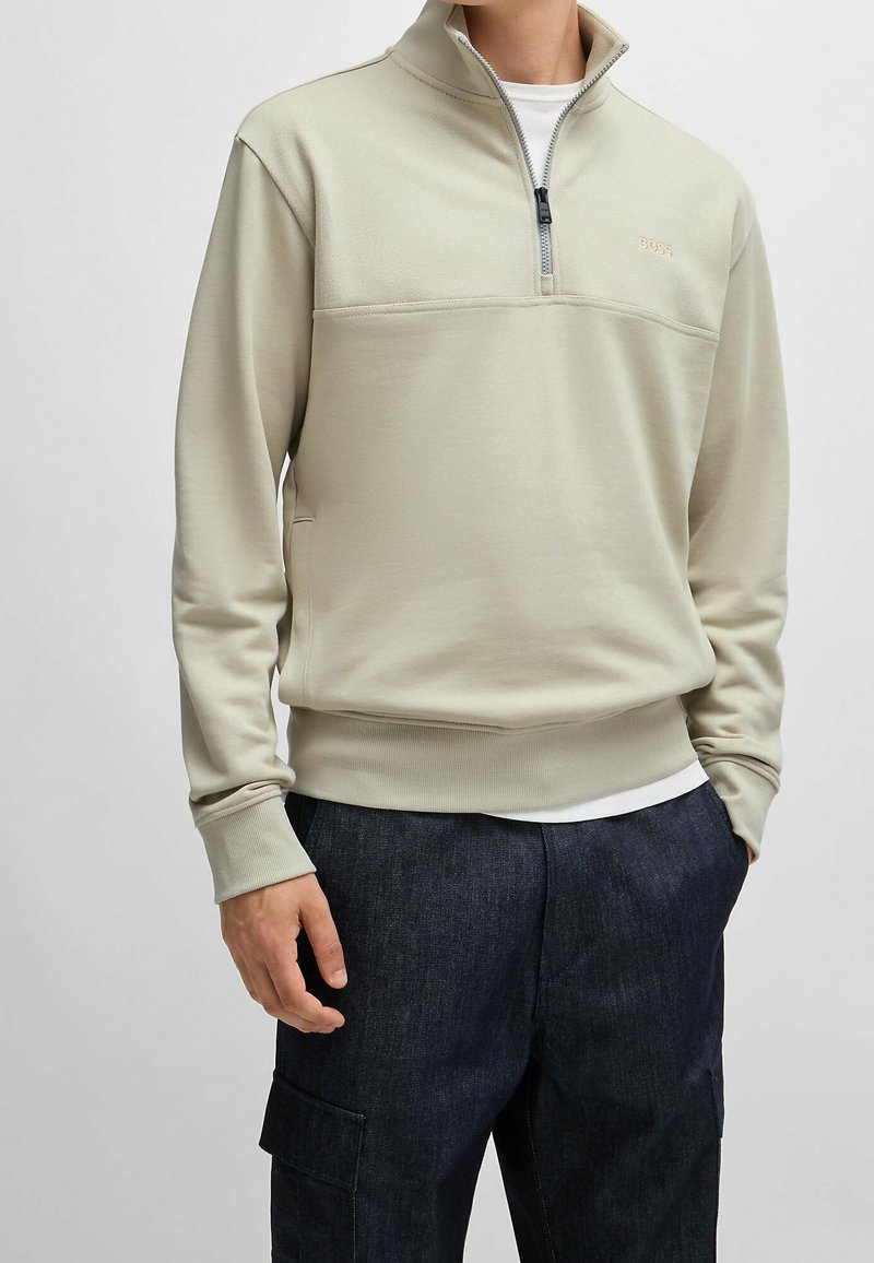 Ljusgrå kvartdraget sweatshirt, med en texturerad övre panel, ribbade muddar och en logotypdetalj på bröstet. Kombinerad med mörka byxor.