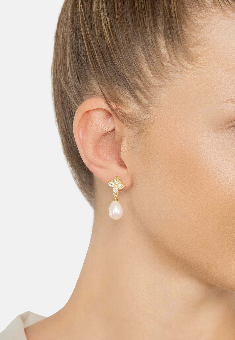 Gold earrings feature a floral design with a pearl drop. The floral part has sparkling accents, creating a contrasting texture.