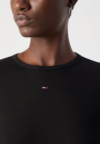 Black ribbed t-shirt featuring a round neckline and a small embroidered logo with red, white, and blue accents on the chest.