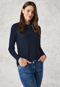Maglia a maniche lunghe blu navy con motivo a maglia testurizzato, scollatura a girocollo e polsini aderenti, abbinata a jeans in denim azzurro.