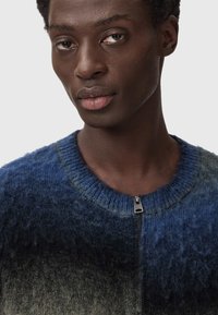 Pleteni pulover z modrim prelivom, z okroglim izrezom in zadrgo. Mehak teksturiran material z puhasto končno obdelavo.