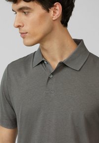 Polo gris en tissu doux avec un col classique, une patte de boutonnage à trois boutons et des manches courtes agrémentées de détails de couture subtils.