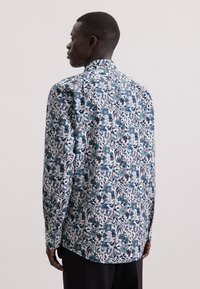 Camicia a maniche lunghe in tessuto bianco con una stampa floreale colorata in tonalità di teal, blu navy e bordeaux; colletto button-down e vestibilità comoda.