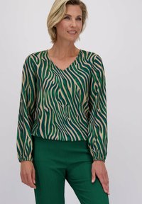 Langsleeve blouse met een groen en beige golvend streepjespatroon, V-hals en elastische manchetten, gecombineerd met textuurover groene broek.