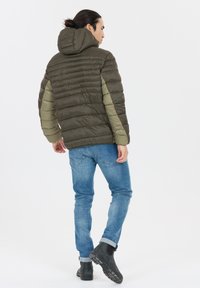 Brun polstret jakke med grågrønne ærmer, hætte og lodret syning. Båret med blå jeans og sorte ankelstøvler mod en hvid baggrund.