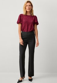 Bordeaux blonde bluse med korte puffærmer, parret med høj talje sorte bukser. Sorte spidse hæle fuldender outfittet.