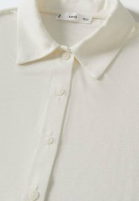 Kremowa koszulka polo wykonana z miękkiej, teksturowanej tkaniny. Posiada klasyczny kołnierzyk oraz pięć guzików na przodzie. Prosty, elegancki design.