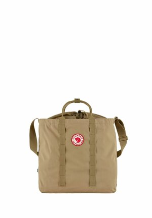 Beige Fjallraven Tragetasche mit zwei Griffen, verstellbarem Schultergurt, Kordelverschluss und rundem roten Logo vorne.