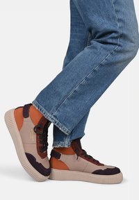 High-top sneakers featuring a mix of beige, brown, and dark purple materials, with a textured rubber sole and black laces.