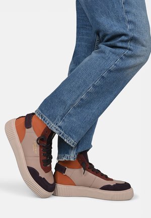 Sneaker alte realizzate con una combinazione di materiali beige, marrone e viola scuro, dotate di una suola in gomma testurizzata e lacci neri.