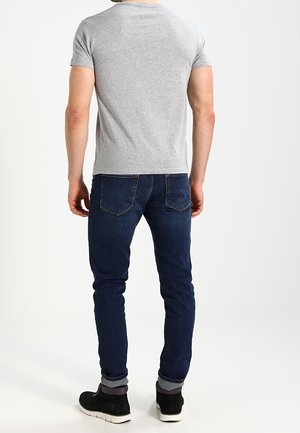 Grå t-shirt med korte ærmer, kombineret med mørkeblå smalle jeans og sorte sko; minimalistisk design, blød tekstur, ensfarvet.