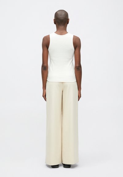 Biely rebrovaný top bez rukávov v kombinácii so širokými béžovými nohavicami, ktoré majú hladkú textúru a jednoduchý dizajn, zobrazené zo zadnej strany.